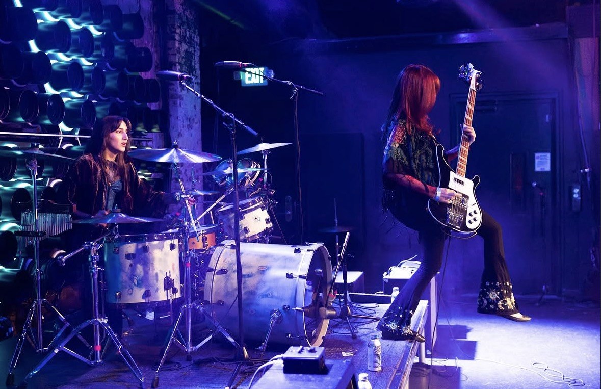 Mónica behind the kit and Mercedes on bass, lit blue
