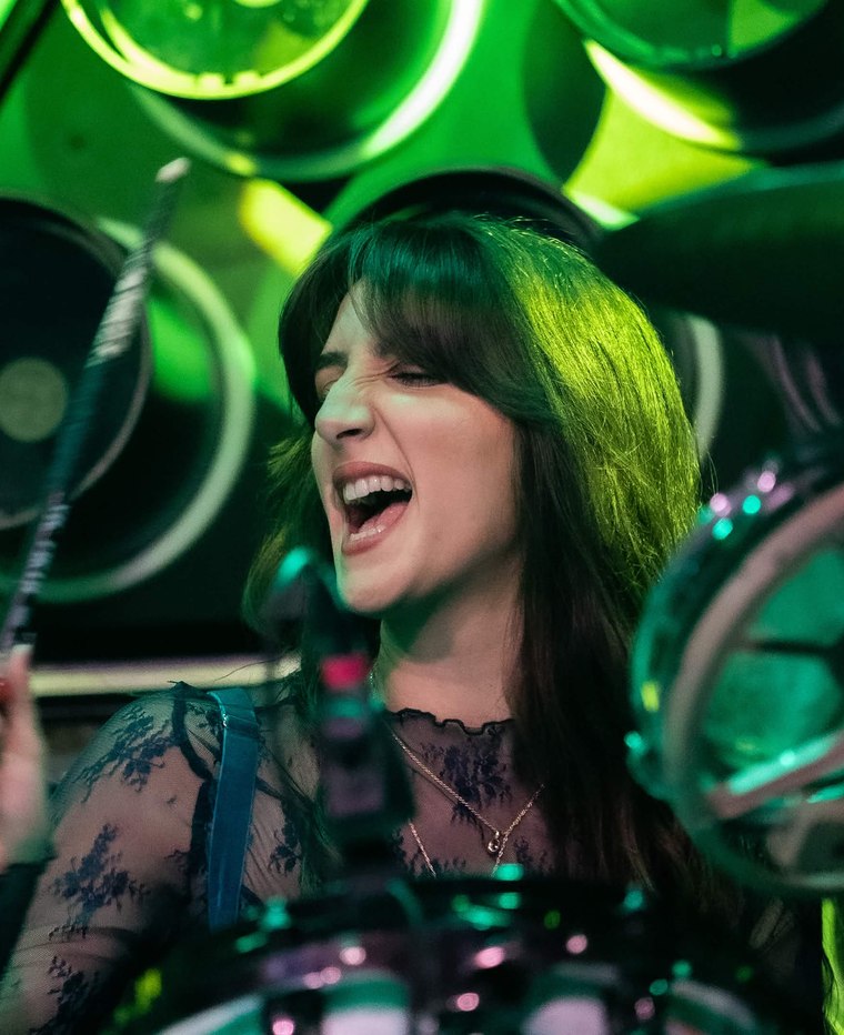 Mónica of Söūp singing behind the kit under green stage light